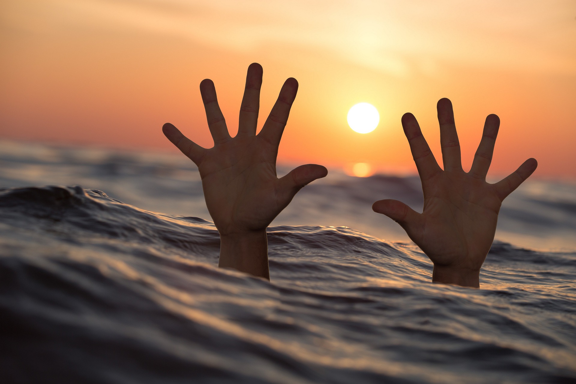 A person in the ocean reaching their hands up
