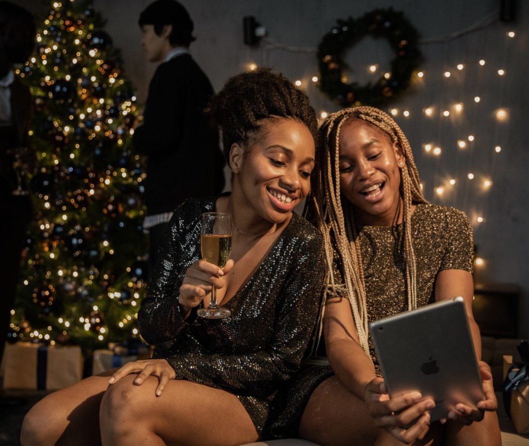 two women looking at an ipad and smiling, sat in front of a christmas tree