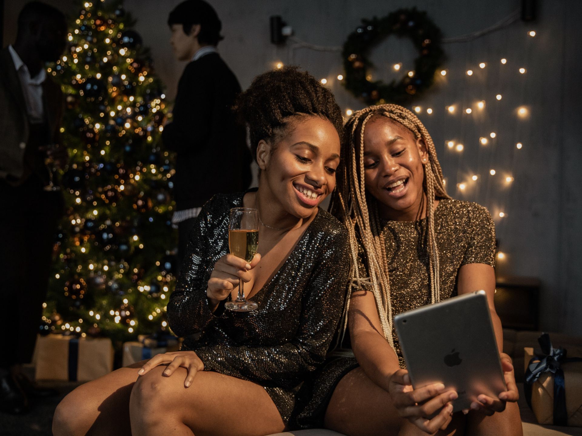 two women looking at an ipad and smiling, sat in front of a christmas tree