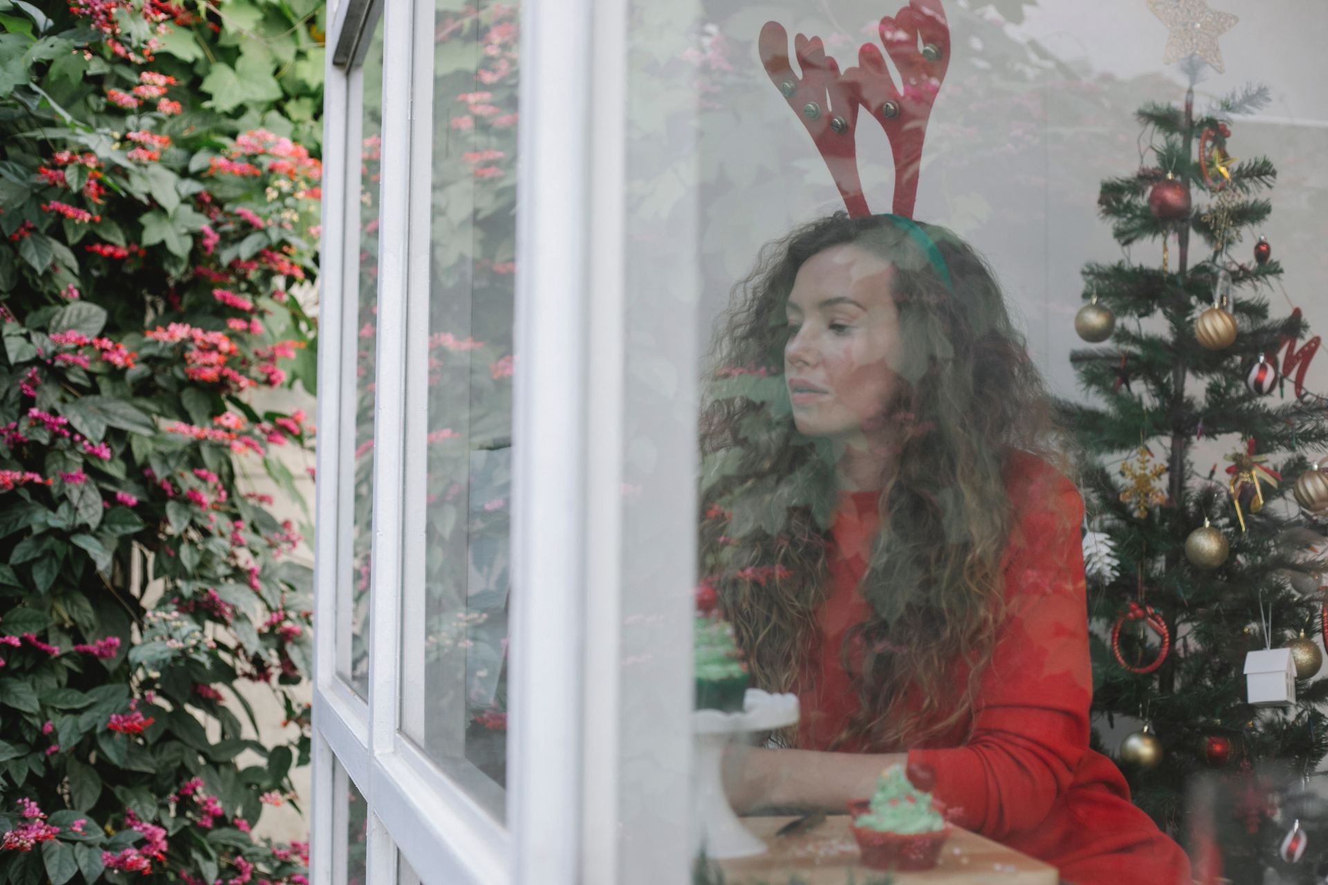 A woman in a christmas setting looking out a window sadly