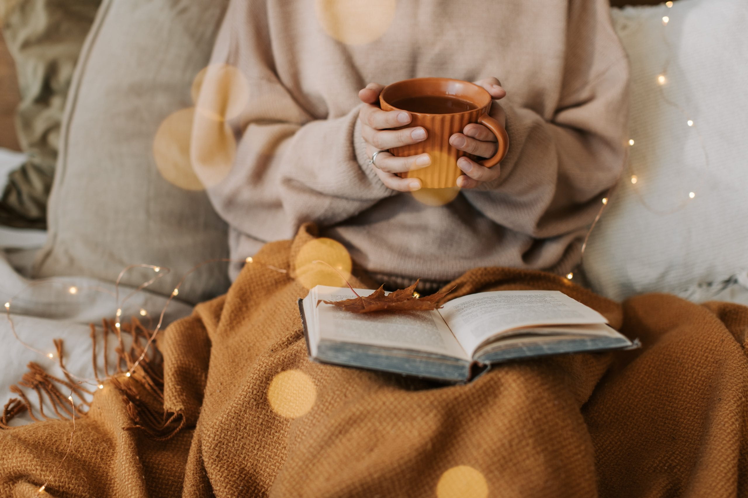 woman with a cup of tea and a book in a blanket