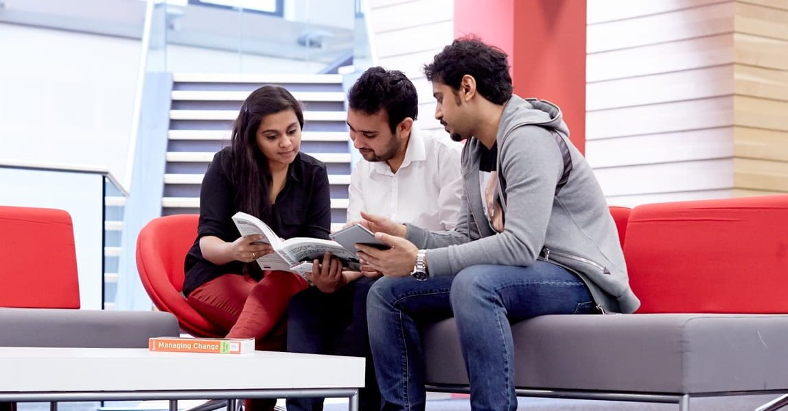 Three students sitting on a couch discussing a book.